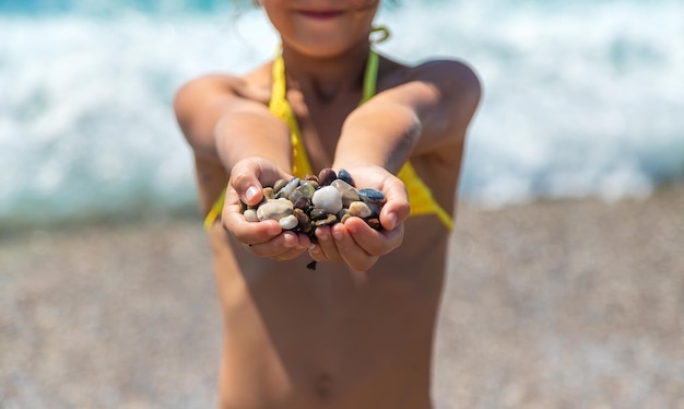 Un bambino sulla spiaggia tiene in mano dei sassi di mare. Messa a fuoco selettiva.