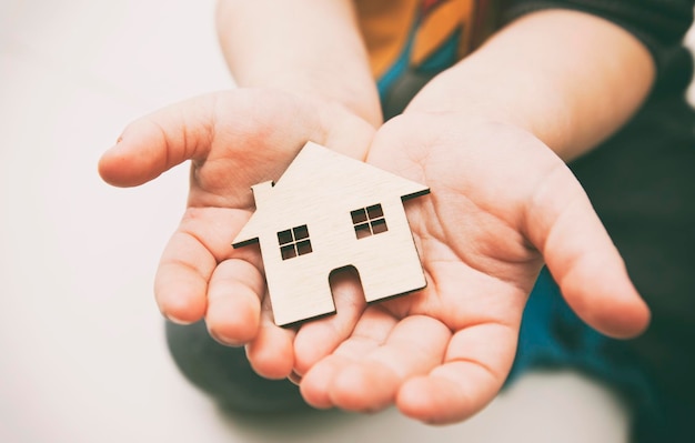 Un bambino tiene in mano una casa piatta di legno sullo sfondo bianco