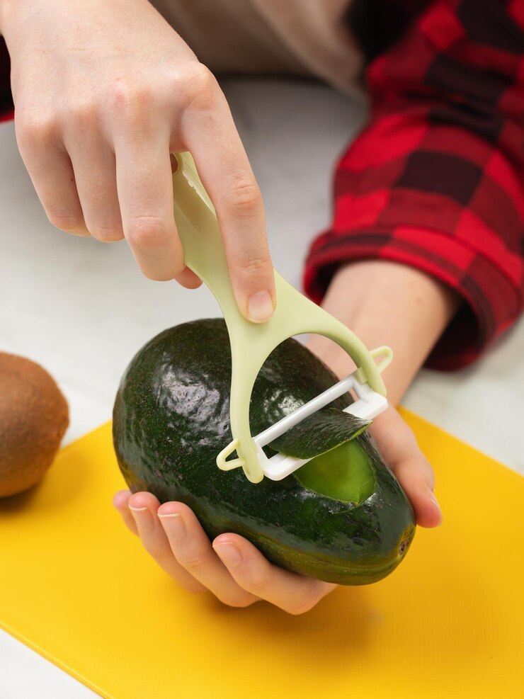 Un bambino tiene un avocado in una mano e sbuccia la pelle con un sbucciatore di verdure con l'altra