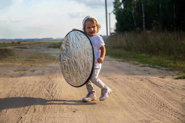 un bambino tiene un riflettore per il fotografo sulla strada di campagna. piccolo aiutante assistente