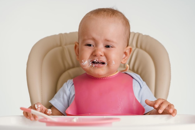 Un bambino urlante si siede su un seggiolone con un bavaglino rosa e si rifiuta di mangiare