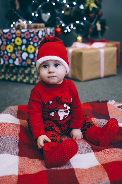 Un bambino vestito da Babbo Natale siede sotto un albero di Natale