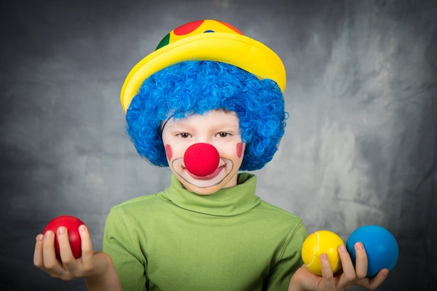 Un bambino vestito da clown con parrucca e naso finto si diverte a giocare con palline colorate per celebrare il carnevale