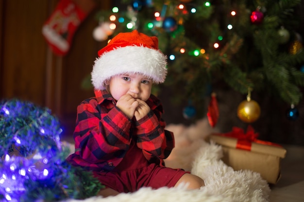 Un bambino vestito di rosso è seduto in attesa del nuovo anno. il concetto di celebrare il Natale a mezzanotte. costume da festa