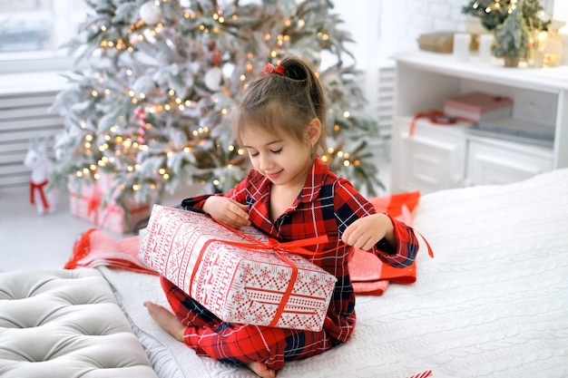 Un bambino vestito in pigiama a letto scioglie un fiocco su un grande regalo di Natale