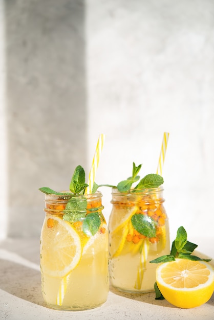 Un barattolo di limonata fatta in casa con limone, bacche e menta su uno sfondo chiaro, luce del sole