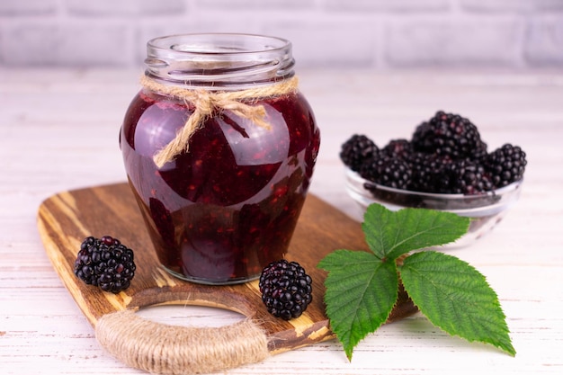 Un barattolo di marmellata di more su uno sfondo di legno bianco.