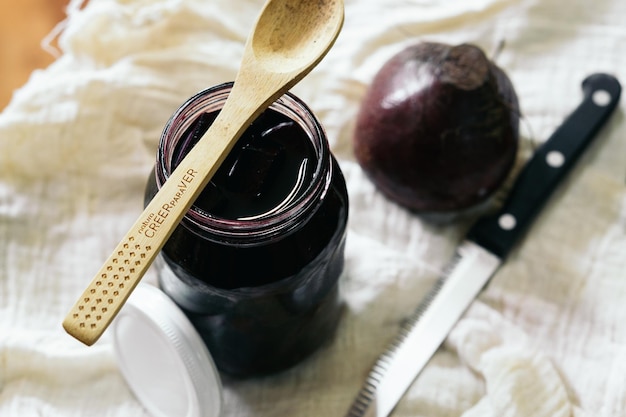 Un barattolo di marmellata viola con un cucchiaio sopra accanto a un coltello e un coltello.