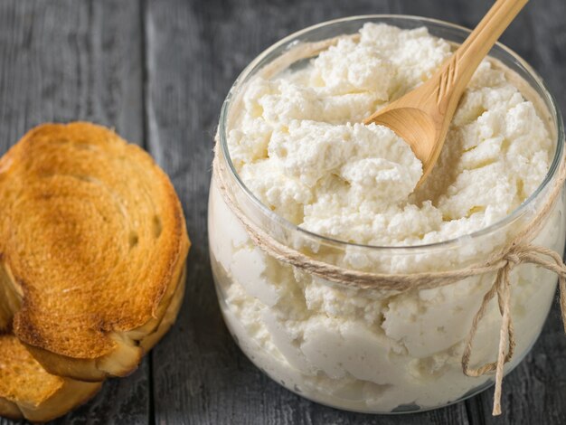 Un barattolo di ricotta e due pezzi di pane tostato su un tavolo di legno. Il concetto di una dieta sana.