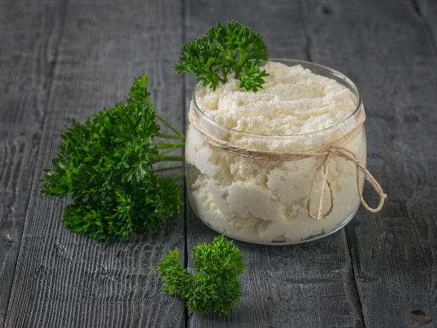 Un barattolo di ricotta fresca con prezzemolo riccio su un tavolo di legno.