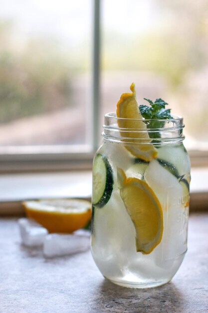 un barattolo di vetro con acqua, limone, cetriolo e menta su un tavolo di marmo, sfondo sfocato