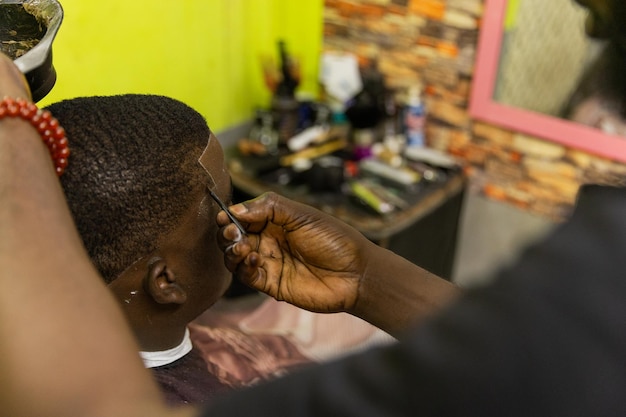 Un barbiere africano applica la tintura per i capelli al suo cliente nel barbiere