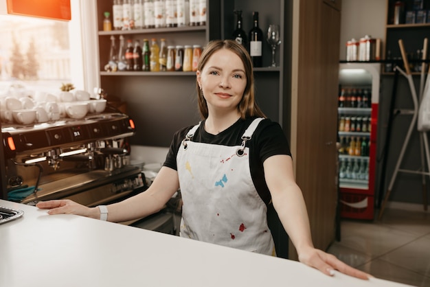 Un barista con un grembiule bianco pone dietro il bar in un bar