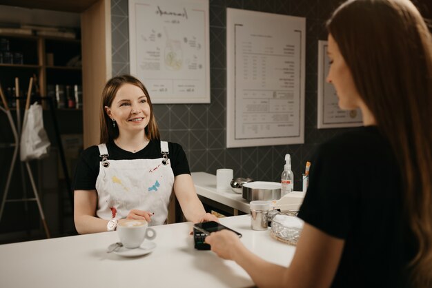 Un barista femmina che sorride dà a un cliente un terminale per pagare in un caffè.