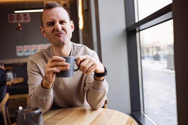 Un bel giovane sorridente e calmo si siede in un bar a un tavolo a bere caffè mentre è seduto a un tavolo in un ristorante. Caffè del mattino