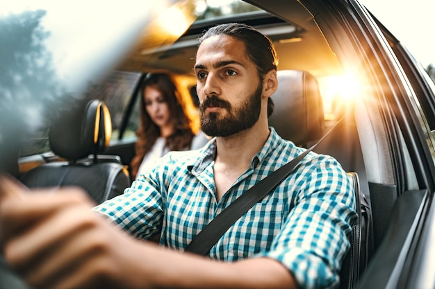 Un bel giovane uomo d'affari sta guidando un'auto in viaggio d'affari e una giovane donna è seduta sul sedile posteriore.