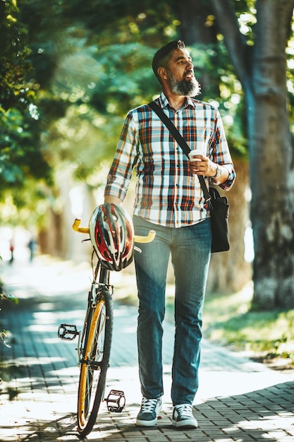 Un bel giovane va in giro in città con la sua bicicletta, camminando con il caffè accanto e pensando a dove sarebbe andato.