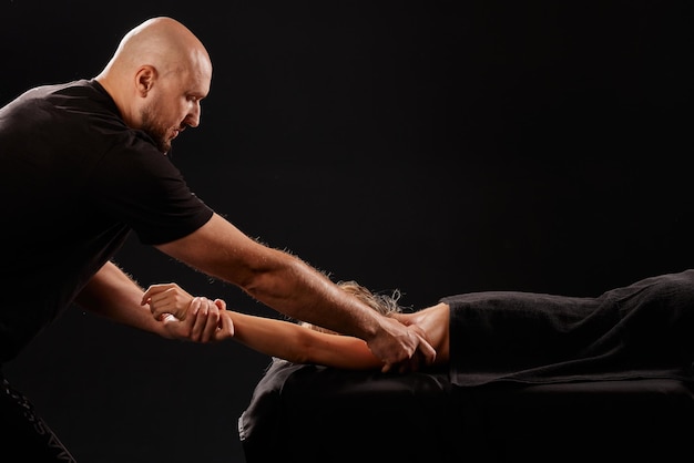 un bel massaggiatore maschile che massaggia una ragazza su sfondo nero concetto di massaggio terapeutico rilassante