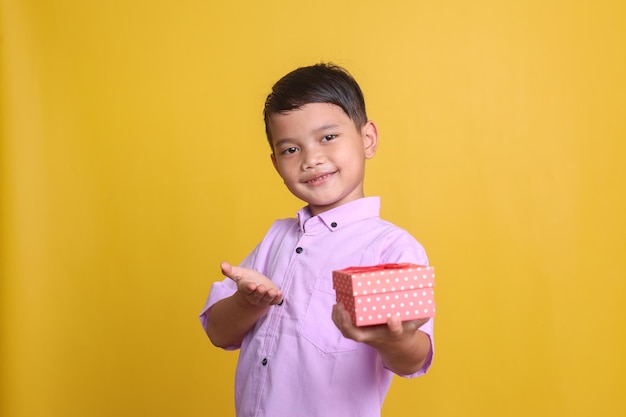 Un bel ragazzino asiatico che mostra una scatola regalo con un'espressione felice isolata sullo sfondo giallo