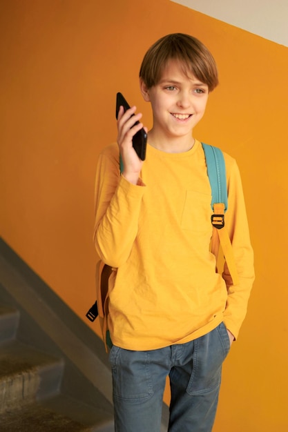 Un bel ragazzo adolescente felice con una maglietta gialla che parla al telefono vicino a un muro giallo