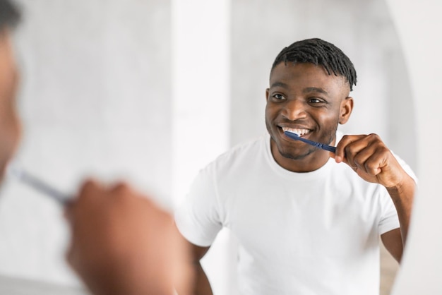 Un bel ragazzo afroamericano millenario che si lava i denti in un bagno moderno.