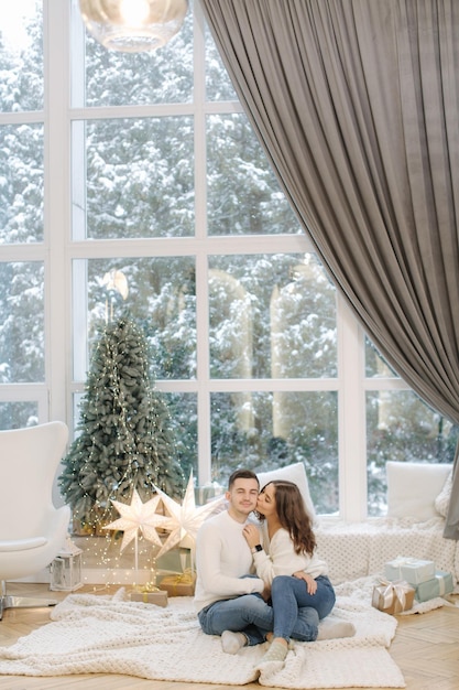 Un bel ragazzo con la sua bella ragazza si abbraccia a casa alla vigilia di natale in forma albero e neve