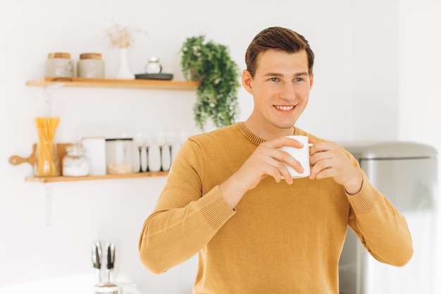 Un bel ragazzo in abiti casual gialli è seduto a casa in cucina a bere caffè