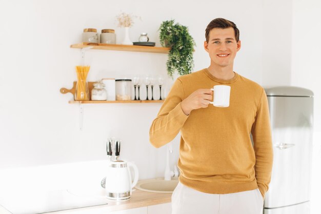 Un bel ragazzo in abiti casual gialli è seduto a casa in cucina a bere caffè