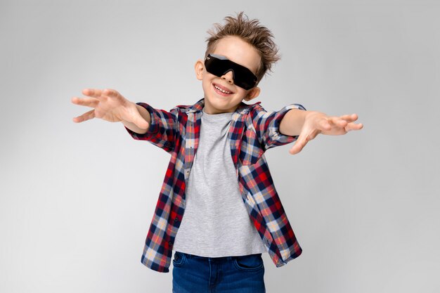 Un bel ragazzo in una camicia a quadri, camicia grigia e jeans si leva in piedi su gray