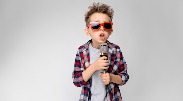 Un bel ragazzo in una camicia a quadri, camicia grigia e jeans si trova sul grigio