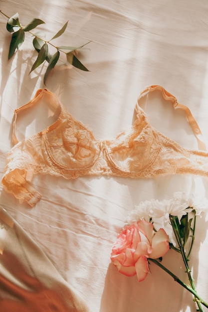 Un bel reggiseno di pizzo è sdraiato sul letto al sole del mattino con ombre con un crisantemo rosa e un ramo di eucalipto