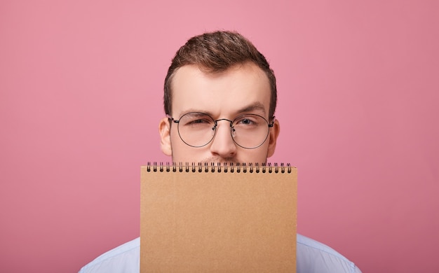 Un bel studente con gli occhiali gli copriva il viso con un quaderno marrone a fogli mobili