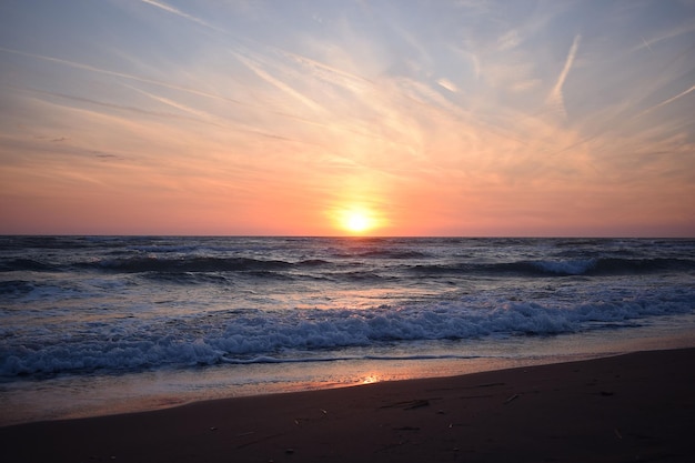 Un bel tramonto sulla spiaggia nell'oceano turbolento Sfumature di arancione e blu