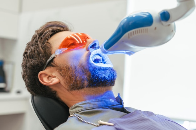 Un bel uomo barbuto sbiancando i denti di un paziente in una moderna clinica dentale