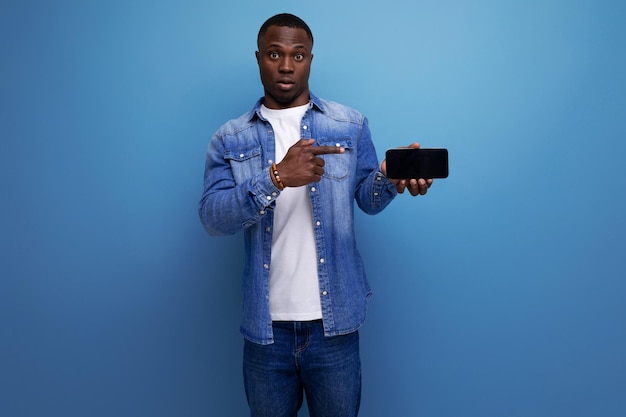 Un bell'uomo americano di un anno con i capelli corti, vestito con stile, mostra lo schermo dello smartphone.