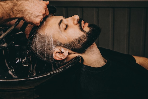 Un bell'uomo barbuto si fa lavare i capelli dal parrucchiere al servizio clienti del barbiere