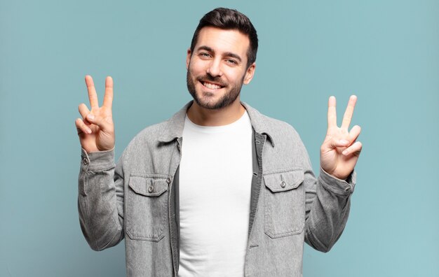 Un bell'uomo biondo adulto che sorride e sembra felice, amichevole e soddisfatto, che indica vittoria o pace con entrambe le mani