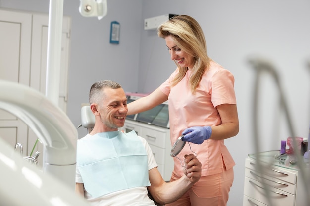 Un bell'uomo caucasico con una dentista esamina i suoi denti allo specchio in una clinica dentale.