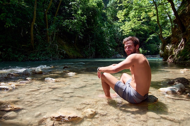 Un bell'uomo caucasico seduto su una roccia in un fiume sotto la luce del sole