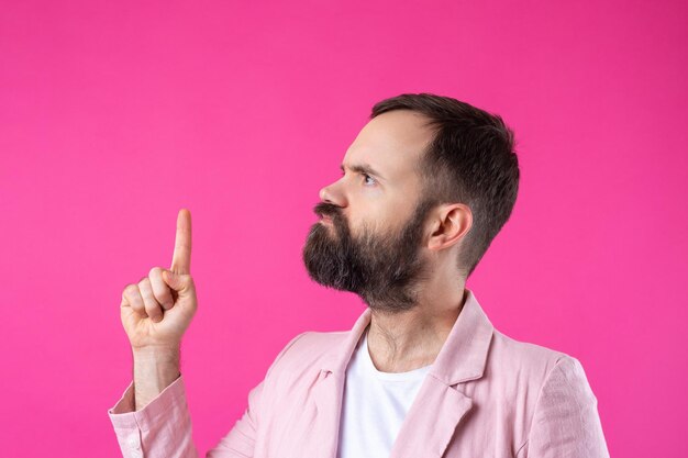 Un bell'uomo con la barba in una giacca rosa sta pensando a uno sfondo rosso isolato