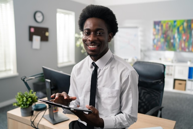 Un bell'uomo d'affari afroamericano del manager dell'azienda con afro si siede alla sua scrivania vestito con un abito