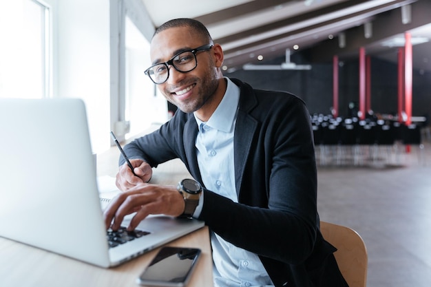 Un bell'uomo d'affari allegro che sorride lavorando al suo computer portatile in ufficio