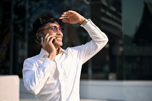 Un bell'uomo d'affari asiatico sta parlando al telefono mentre cammina in una città in una giornata di sole