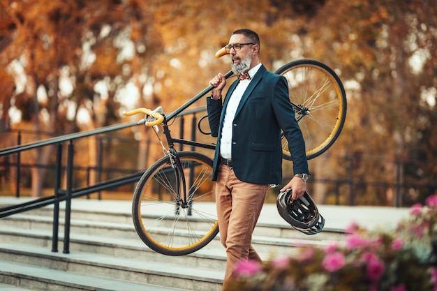 Un bell'uomo d'affari di mezza età casual sta andando in ufficio in bicicletta. Sta portando una bicicletta in spalla sopra le scale.