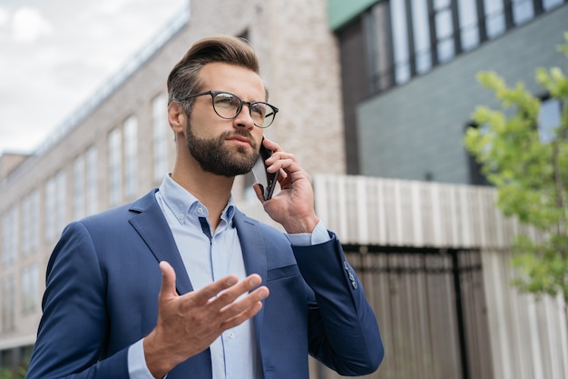 Un bell'uomo d'affari serio che parla al telefono cellulare camminando per strada