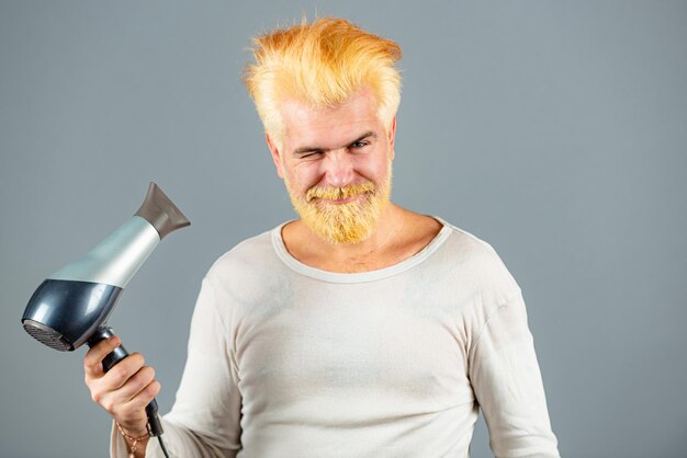 Un bell'uomo dai capelli rossi con i capelli lunghi si asciuga i capelli con un asciugacapelli. Uomo barbuto biondo con asciugacapelli.