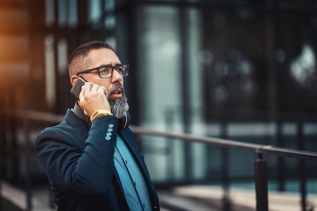 Un bell'uomo di mezza età va al lavoro e parla sullo smartphone davanti al quartiere degli uffici.