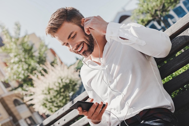 Un bell'uomo farà una telefonata usando gli auricolari si siede su una panchina