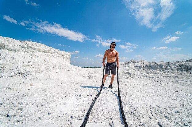 Un bell'uomo forte cammina su una cava Paesaggio bianco Servizio fotografico in una cava Concetto di sport all'aperto Allenamento con le corde