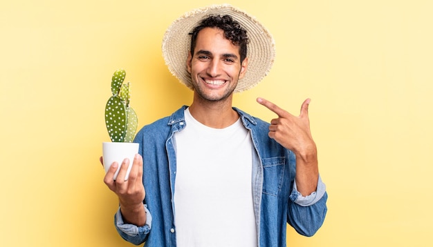 Un bell'uomo ispanico che sorride con sicurezza indicando il proprio ampio sorriso agricoltore e concetto di cactus